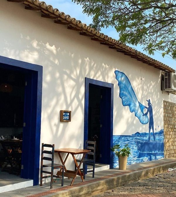 Fachada branca do Pirá com portas emolduradas em azul e mural de um pescador jogando a rede