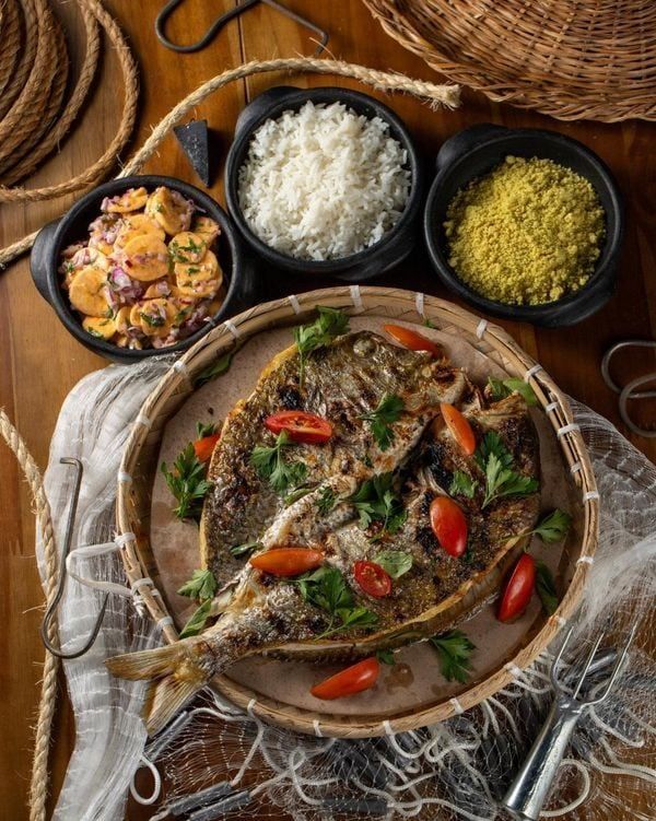 Peixe inteiro assado na brasa servido com arroz branco, farofa e ceviche de banana-da-terra