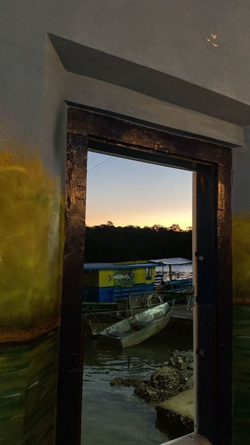 A porta do salão do Pirá aberta para o Rio Benevente ao entardecer, com barcos ancorados no porto